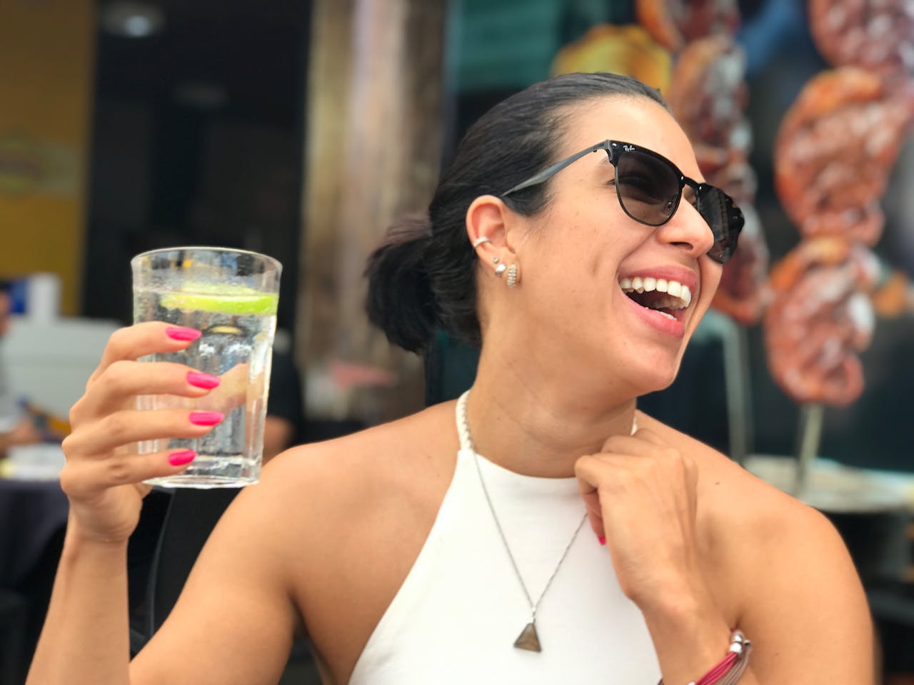 our-story-01 A cheerful woman wearing sunglasses and holding a refreshing drink while enjoying a sunny day.